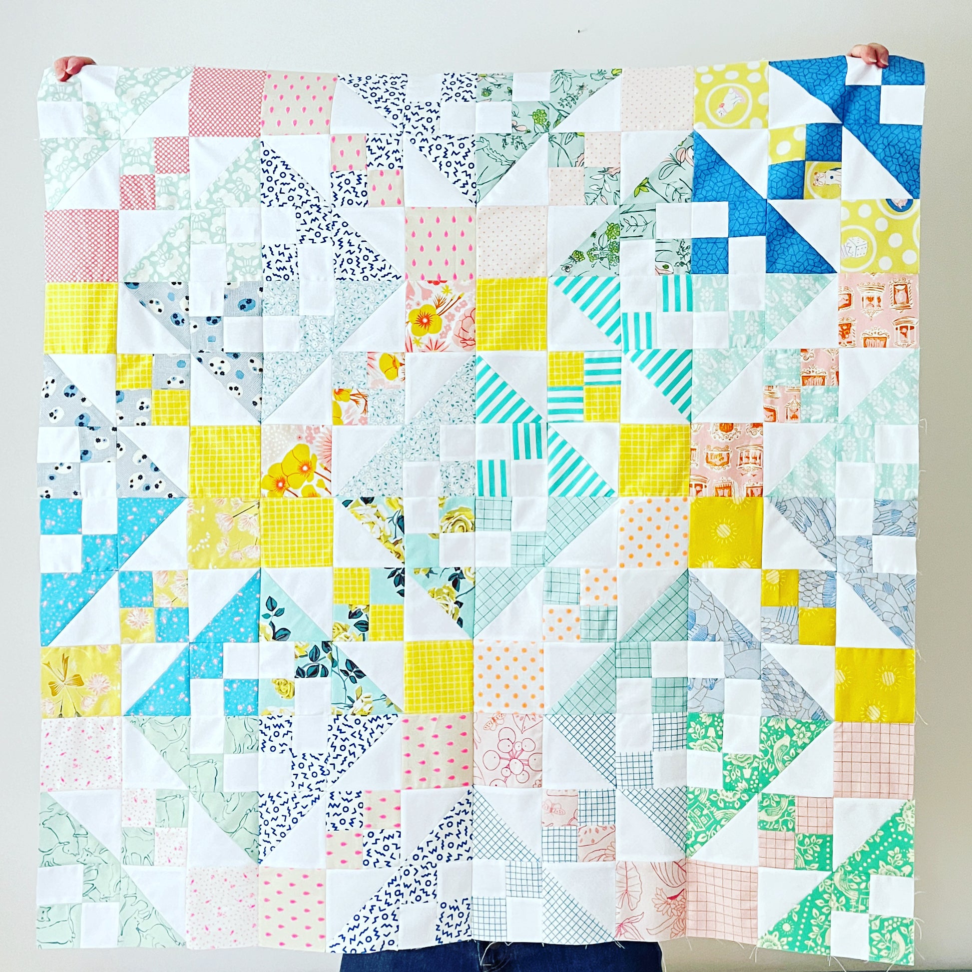 Low volume quilt with geometric patterns held by a person against a white background
