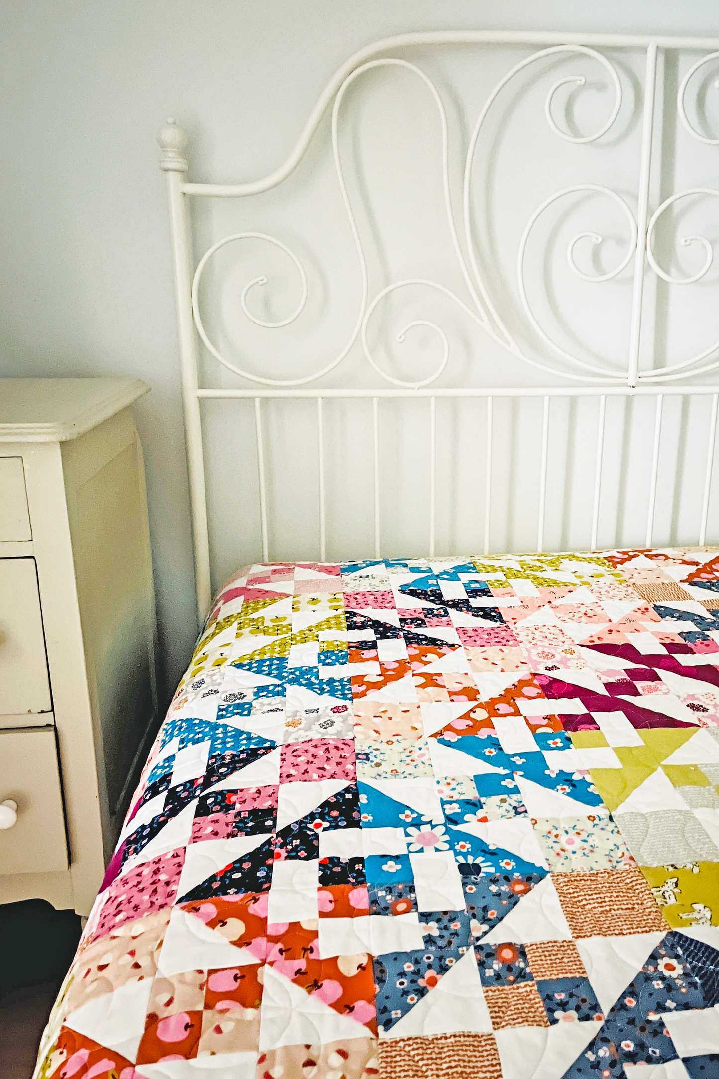 White painted wrought iron bed with a brightly colored sugarcubes quilt