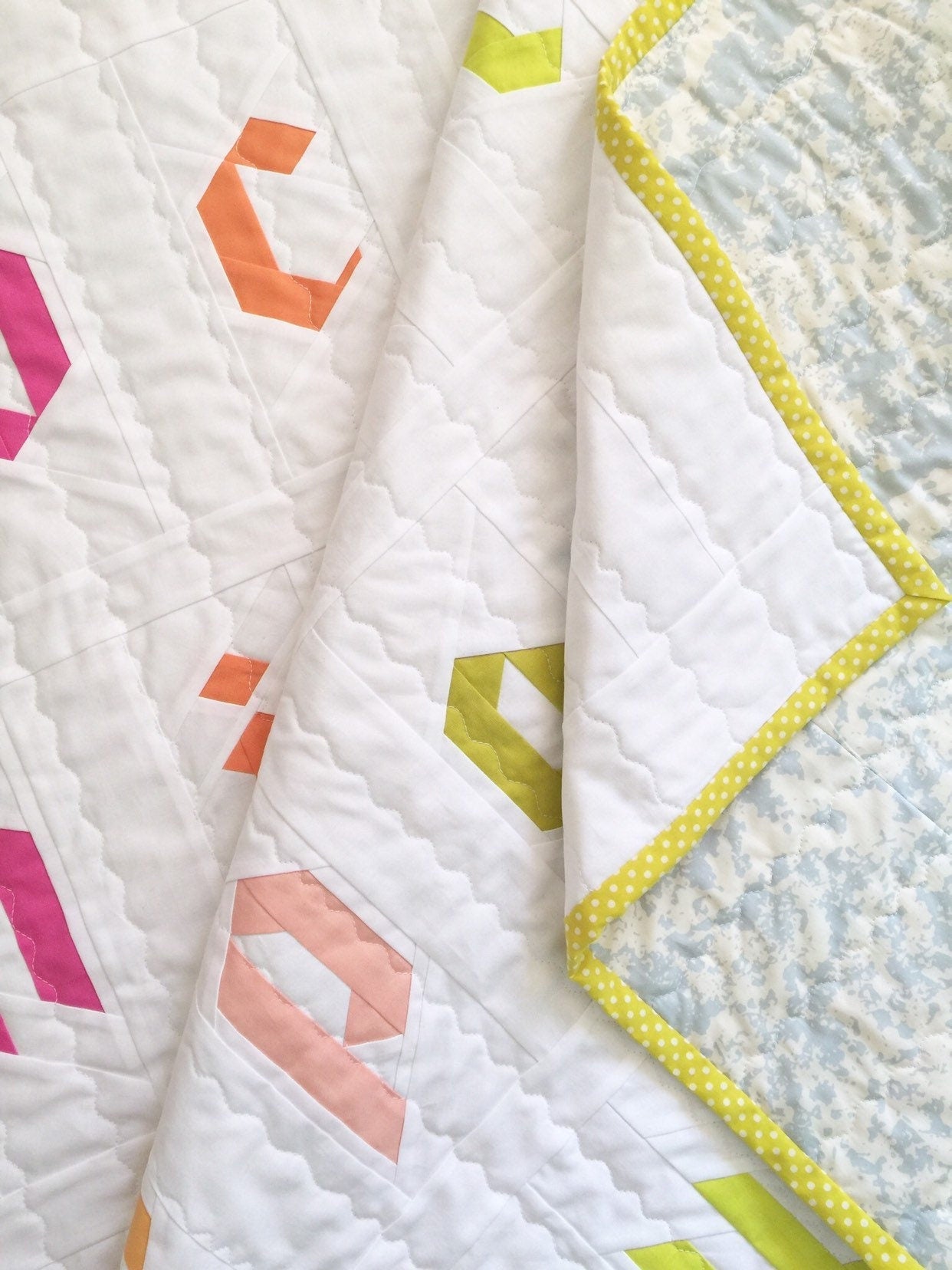 Gently folded quilt showing details of lowercase FPP letters in a soft palette.